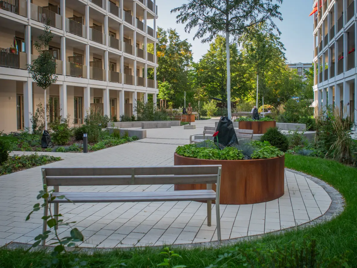 DSW24 – Dresder Servicewohnen GmbH – Augustus Residenz Dresden-Prohlis – begrünter Innenhof Begrünter Innenhof der Augustus Residenz in Dresden Prohlis mit Rasenflächen, Hochbeeten und Aufenthaltsbereichen mit Sitzgelegenheiten.