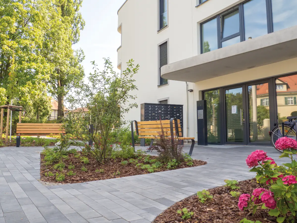 DSW24 – Dresder Servicewohnen GmbH – Eichen Carré Dresden-Niedersedlitz – Eingangsbereich mit Briefkästen und Bänken Eingangsbereich des Eichen Carré in Dresden Niedersedlitz mit Sitzbänken und Briefkästen vor dem Gebäude.