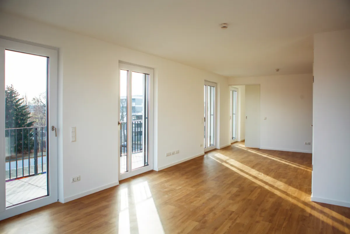 DSW24 – Dresder Servicewohnen GmbH – Eichen Carré Dresden-Niedersedlitz – Wohnbereich Heller Wohnbereich im Eichen Carré in Dresden Niedersedlitz mit Blick auf bodentiefe Fenster, Balkon und angrenzenden Küchenbereich.