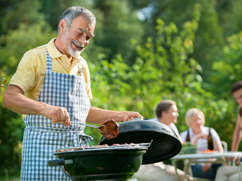 Ein Mann steht am Grill im Grünen und wendet ein Steak.