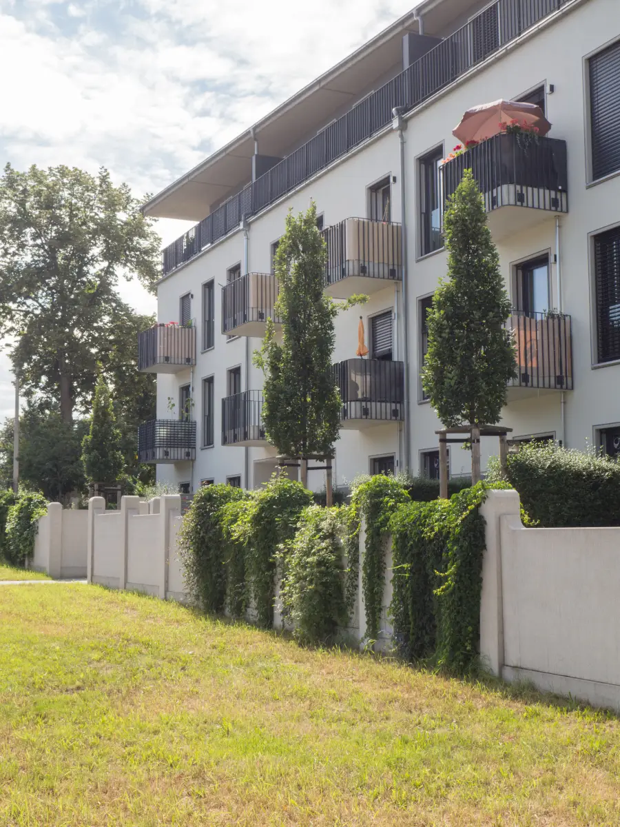 DSW24 – Dresder Servicewohnen GmbH – Rennbahn Residenz Dresden-Seidnitz – Außenansicht mit Mauer Außenansicht der Rennbahn Residenz in Dresden Seidnitz mit Balkonen und begrünter Mauer im Vordergrund.